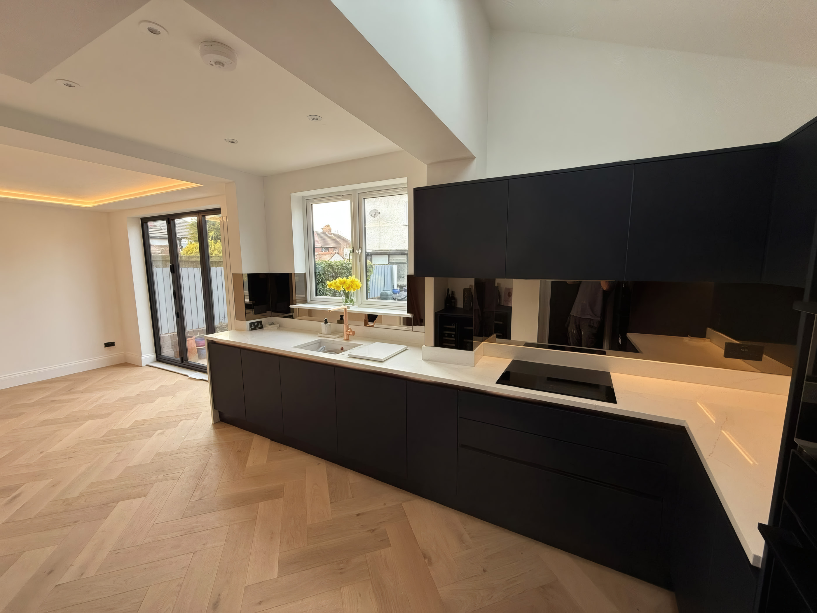 Handleless kitchen with quad integrated ovens and slatted oak ceiling bulkhead in Crosby